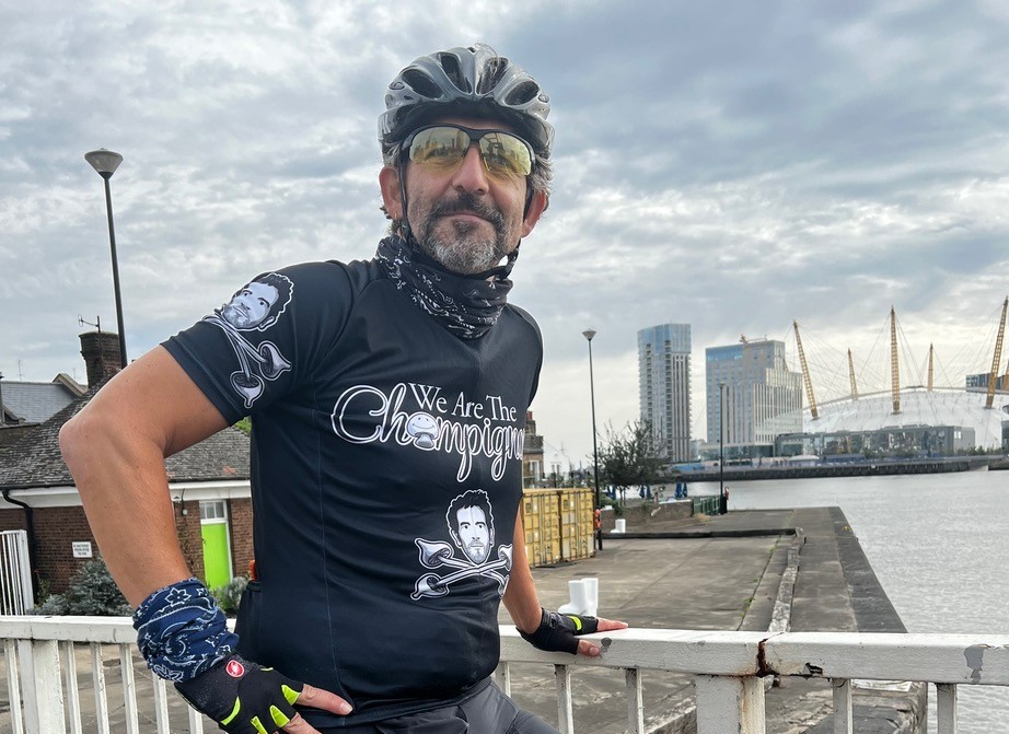 Bowel cancer patient, Dick Carruthers, on his bike in cyling top, gloves and helmet. Pictured with the River Thames and the O2 arena in the background.