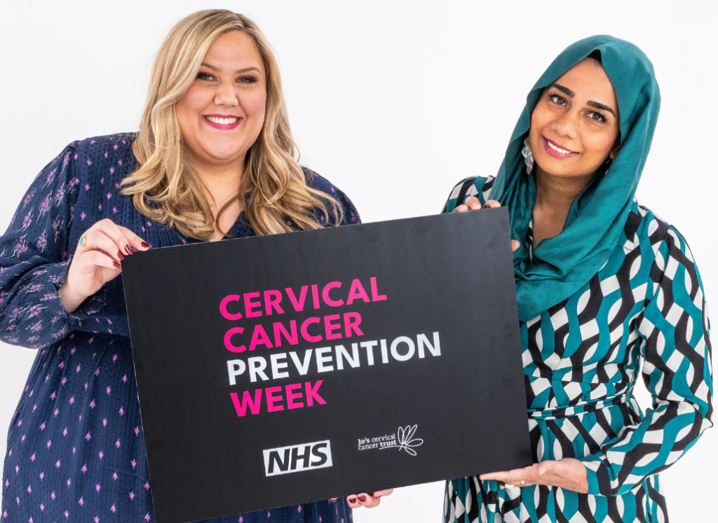 Laura Adlington (left) and Dr Nighat Arif stand together holding a banner between them. It says Cervical Cancer Prevention Week and includes the NHS and Jo's Cervical Cancer Trust logos.