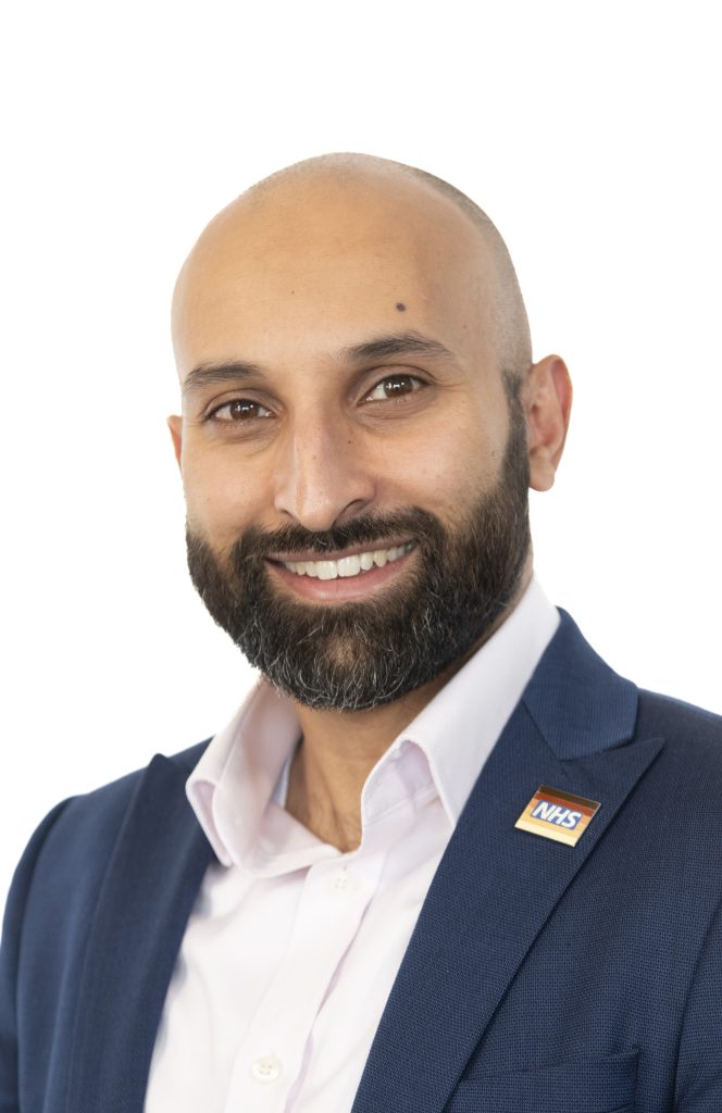 Ali Malik, Managing Director, North Central London Cancer Alliance in open-necked white shirt and dark blue jacket