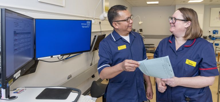 Two cancer clinical nurse specialists in dark blue uniforms, standing next to a computer screen, in friendly discussion