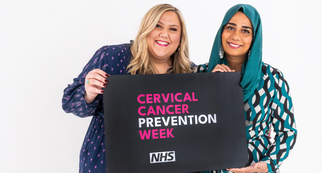 Laura Adlington (left) and Dr Nighat Arif stand together holding a banner between them. It says Cervical Cancer Prevention Week and includes the NHS logo.