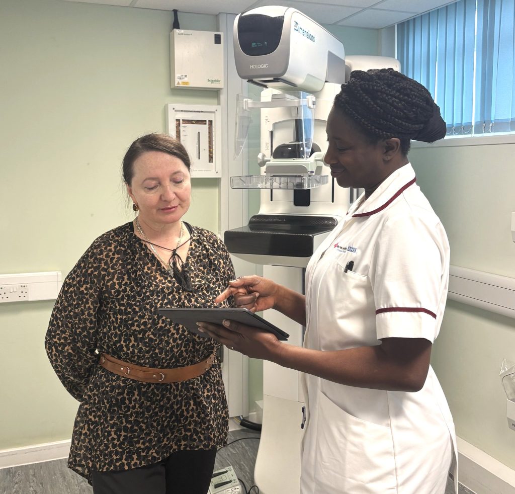 A nurse points to an iPad to explain breast cancer screening to a patient in her native language.