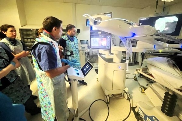 Surgical theatre with robotic bronchoscopy equipmemt and three clinicians viewing.