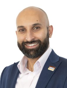 Ali Malik, Managing Director, North Central London Cancer Alliance in open-necked white shirt and dark blue jacket